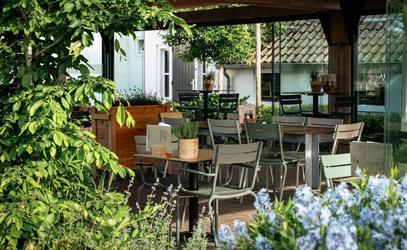 een terras in de zon met bloemen en licht groene stoelen